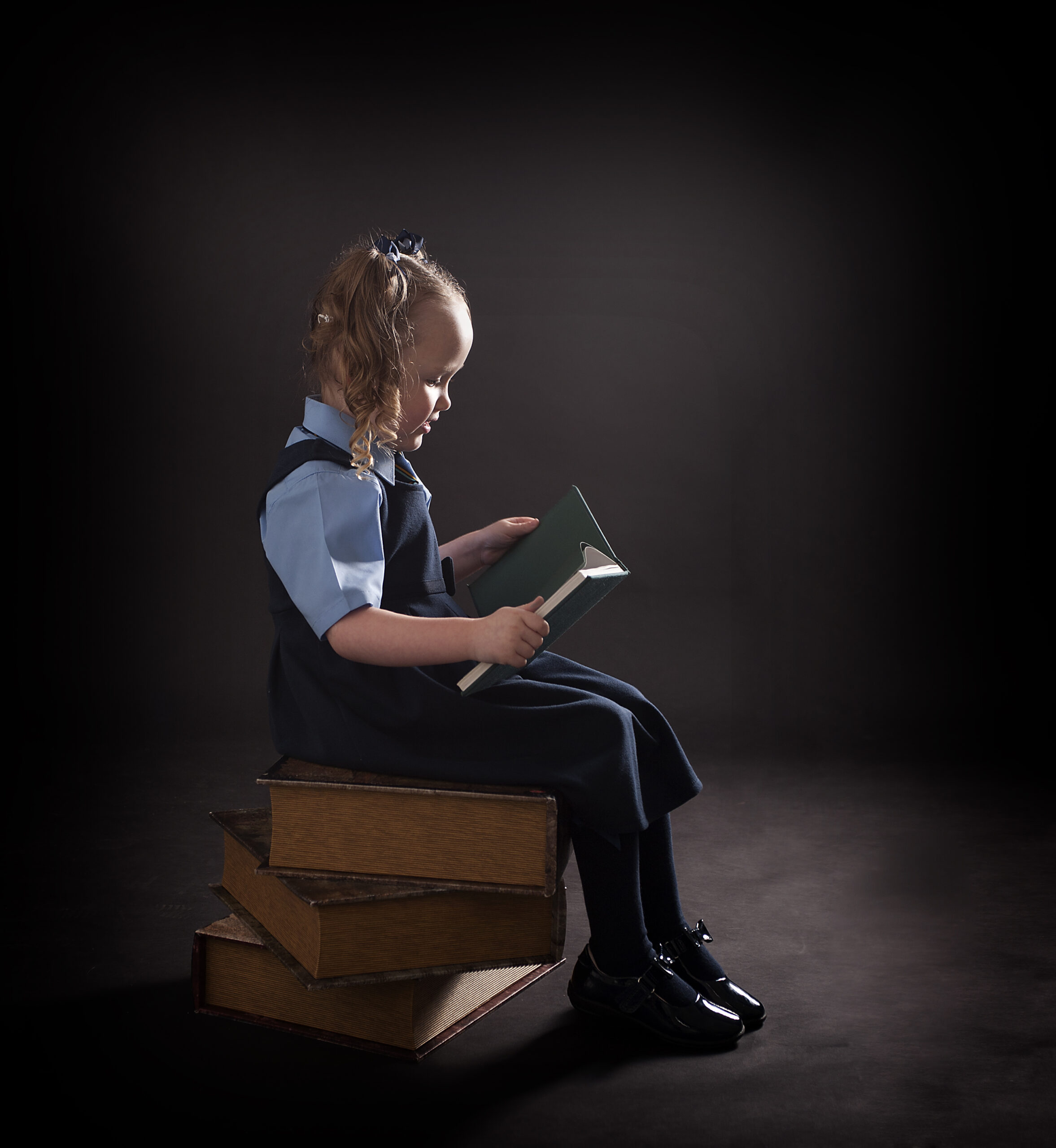 girl in school uniform reading a book on a pile of books