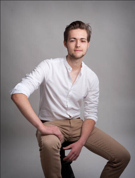 actor , headshot, sitting on a stool, white shirt
